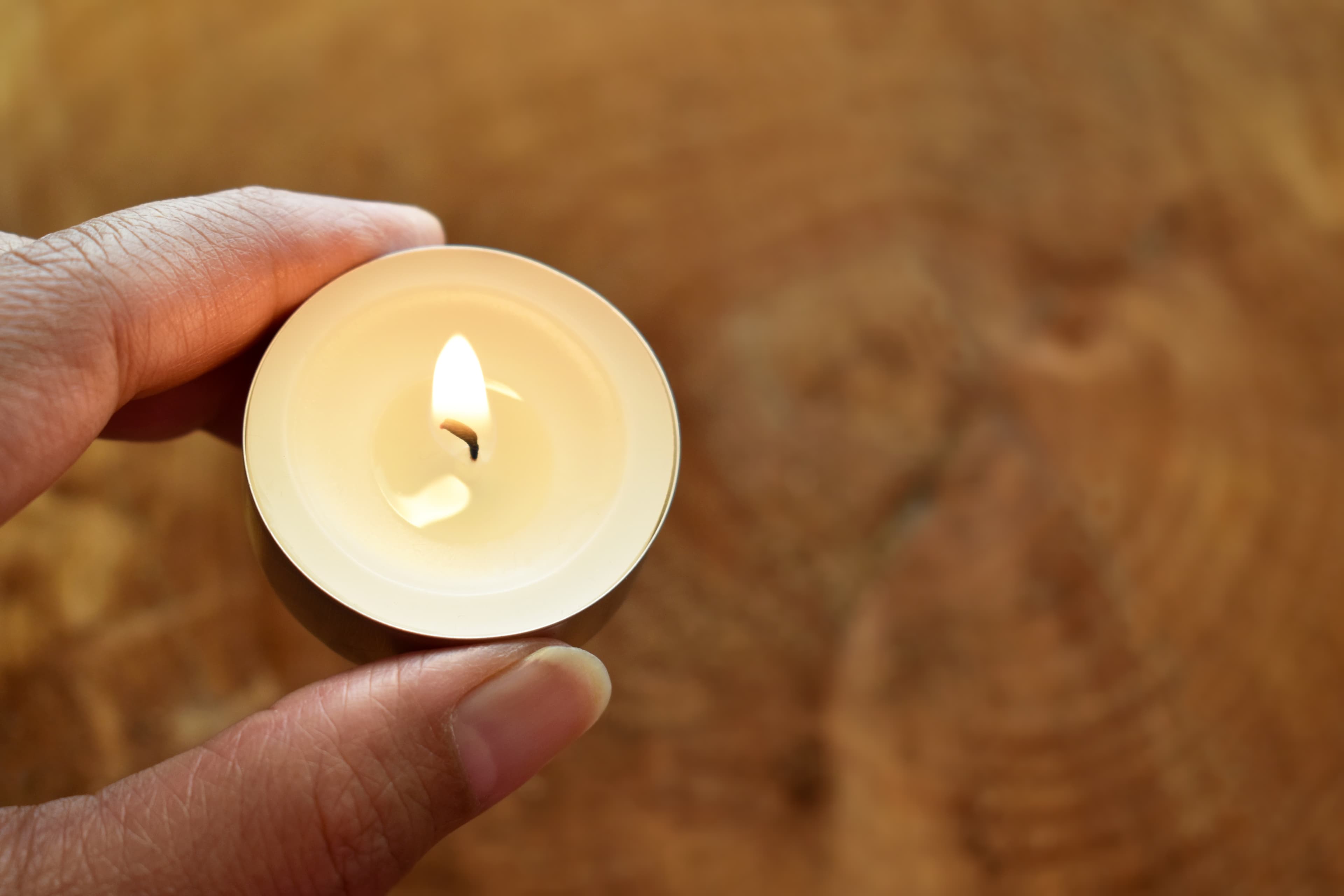 Person holding a lit tea light over a wooden table