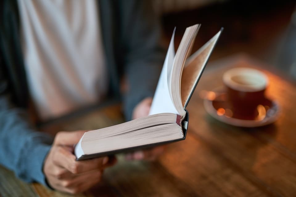 Person sitting at a table reading a hardback book